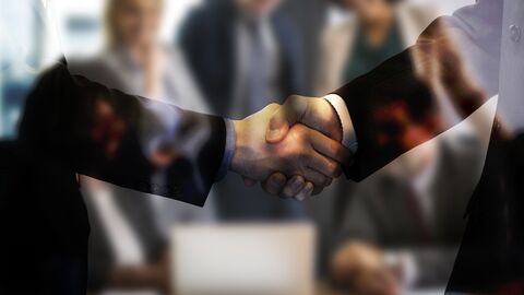 Vermittlung Handschlag zweier Personen, im Hintergrund befinden sich weitere Menschen, die verschwommen sind.