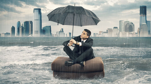 Ein Mann sitzt auf einem Sofakissen auf einem stürmischen Meer und hält einen Schirm hoch