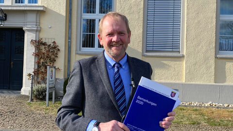 Der Präsident des Rechnungshofs steht vor dem Rechnungshof und hält die Bemerkungen 2020 in die Kamera.