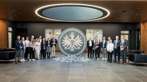 Digitalisierungsworkshop bei der EintrachtTech GmbH Teilnehmende des Digitalisierungsworkshop neben dem Steinlogo der Eintracht Frankfurt